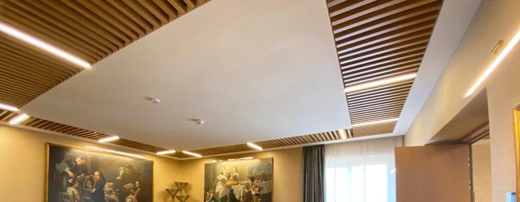 Seamless acoustic plaster ceiling panel framed by timber slats in a meeting room at Banca d’Italia, Rome